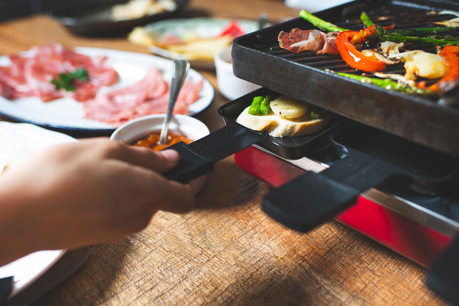 Une main glisse un poêlon de fromage sous la plaque de l'appareil à raclette